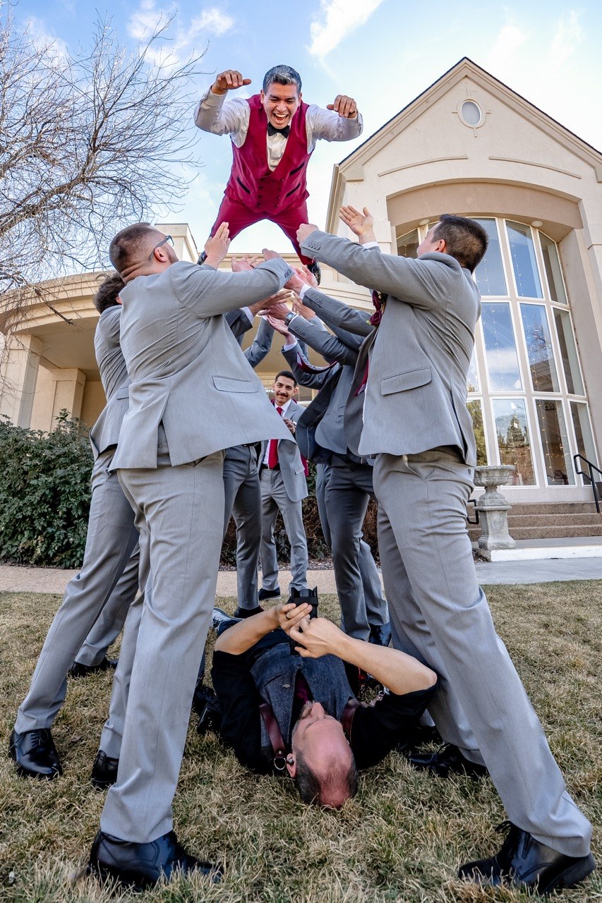 Jeff lying on the grass shooting upward as groomsmen toss the groom into the air