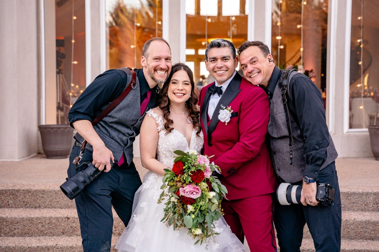 Jeff and a second photographer with their cameras, smiling beside a bride and groom